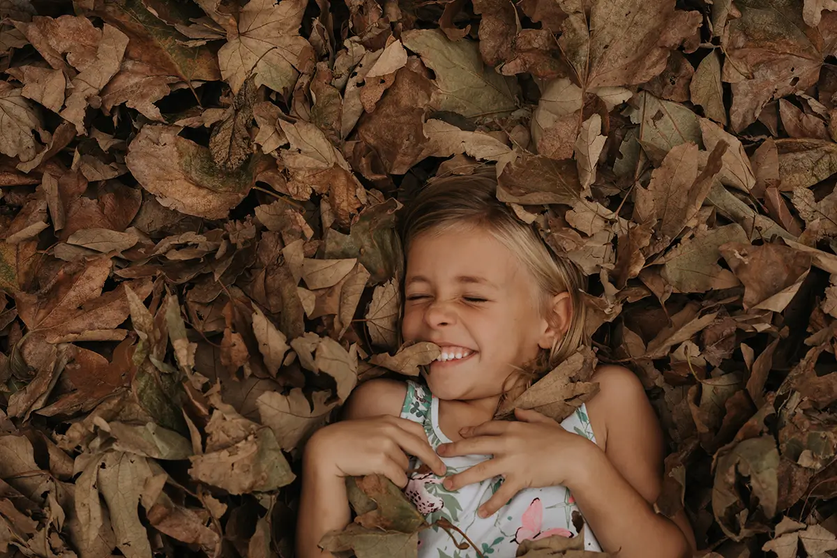 Child having fun with Maple dry leaves fallen on the ground at autumn at the Kartrite