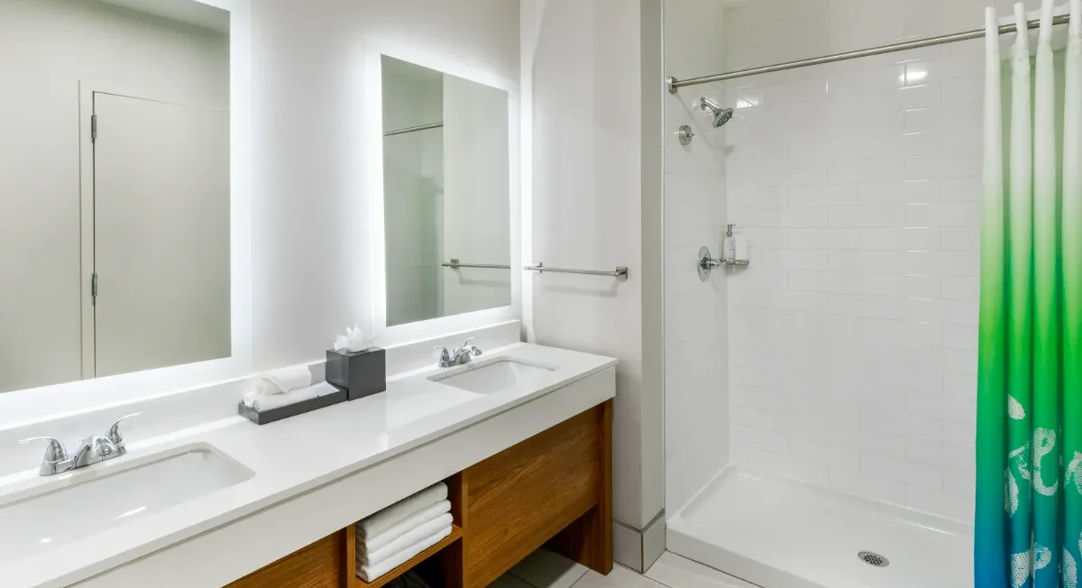 Modern bathroom with double sinks, large mirrors, wooden vanity, open shelving, and a walk-in shower with a green and blue ombre shower curtain.