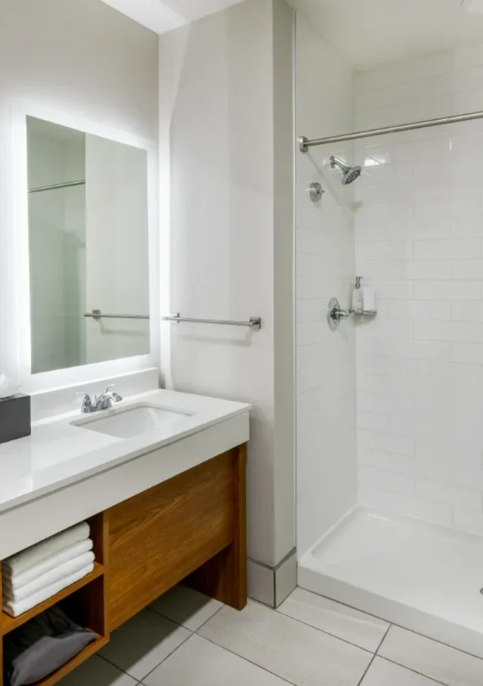 Modern bathroom with double sinks, large mirrors, wooden vanity, open shelving, and a walk-in shower with a green and blue ombre shower curtain.