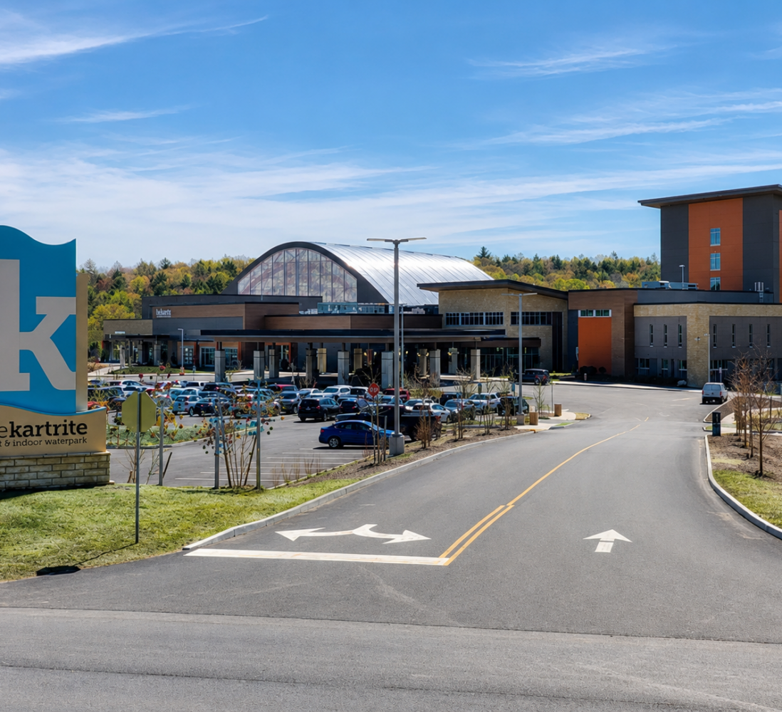 A road leads to a large modern resort with many cars parked outside and a sign reading thekartrite resort & indoor waterpark..