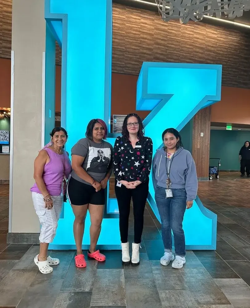 Four women stand smiling in front of a large, blue K sculpture inside a modern building with tile floors and a wood accent wall.