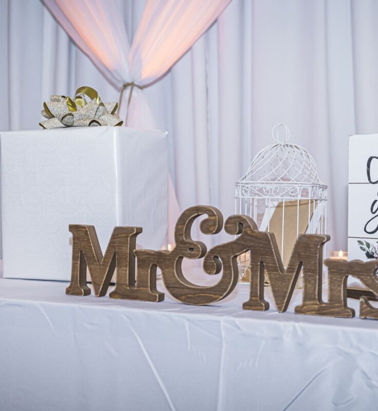 A wedding gift table with a Mr & Mrs sign, wrapped present, birdcage, bouquet, and a Cards & Gifts sign with a floral design.