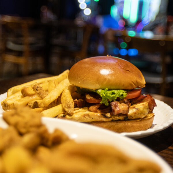 A cheeseburger with lettuce and tomato is served with thick-cut fries on a white plate, with another plate of food blurred in the foreground.
