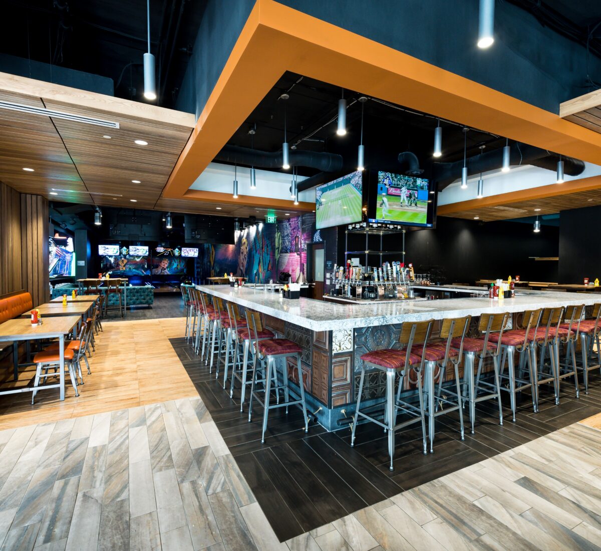 Modern sports bar with a large square marble bar, high chairs, TV screens, wood accents, and booths along the left wall.