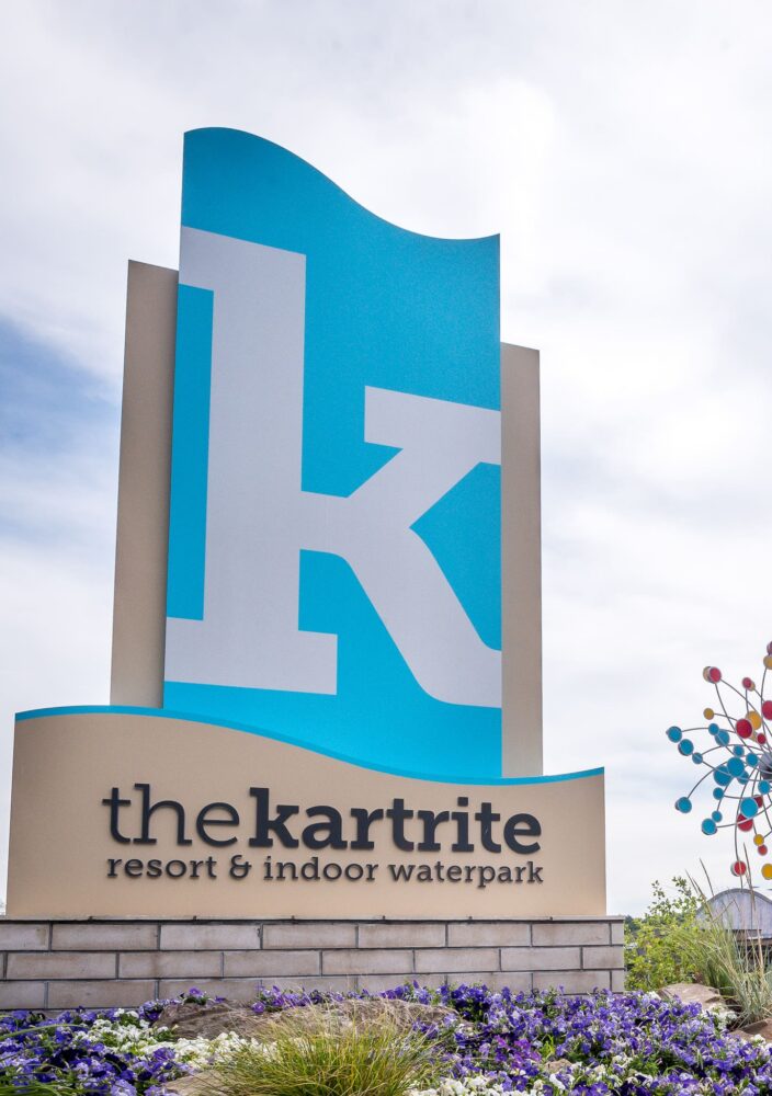 Large blue sign with a white k reads the kartrite resort & indoor waterpark. Modern buildings and colorful sculptures are in the background.