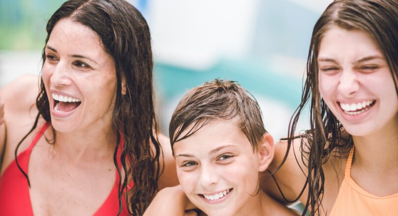 Three people in swimsuits, smiling and standing close together with wet hair, enjoying time at what appears to be a water park or pool.