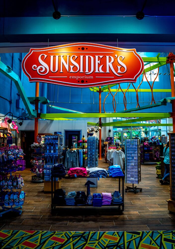 A bright store interior with racks of colorful clothes and souvenirs under a large Sunsiders Emporium sign.