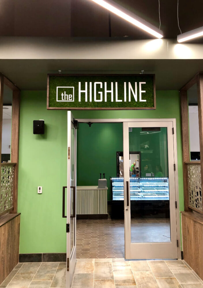 A doorway with glass doors leads to a room with green walls and a sign above reading the HIGHLINE in white letters on a green background.