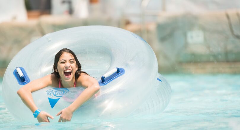 Smiling girl in a pool holds an inflatable tube, enjoying the water on a sunny day.