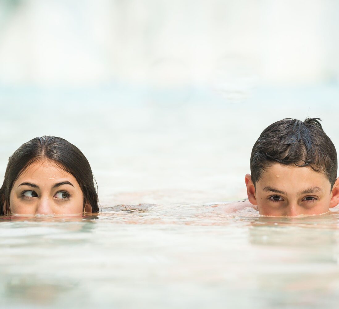 Two kids in a pool, with only their faces visible above the water, looking to the side.