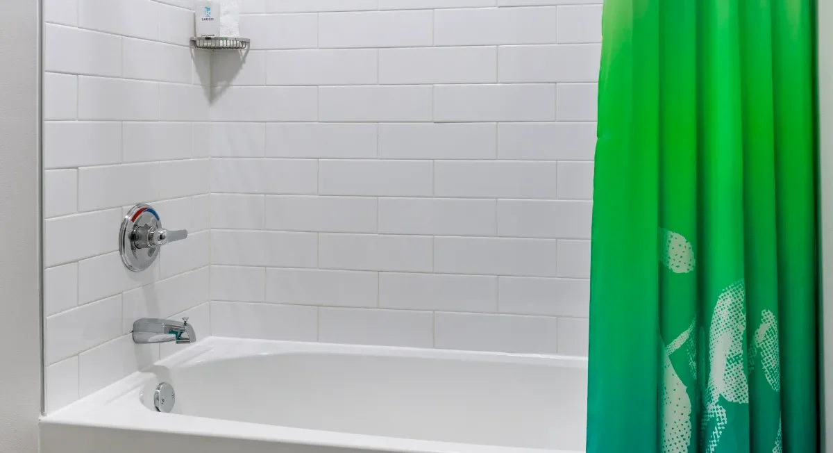 White tiled bathtub with a soap dispenser on a corner shelf and a green ombré shower curtain partially covering the tub.