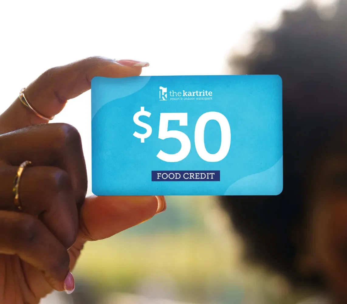A hand holds a $50 food credit card for The Kartrite resort, with a blurred background and soft sunlight.