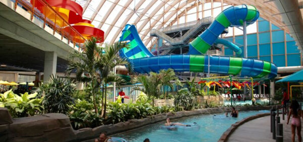 Indoor water park with a lazy river and large blue and green water slides under a glass roof.